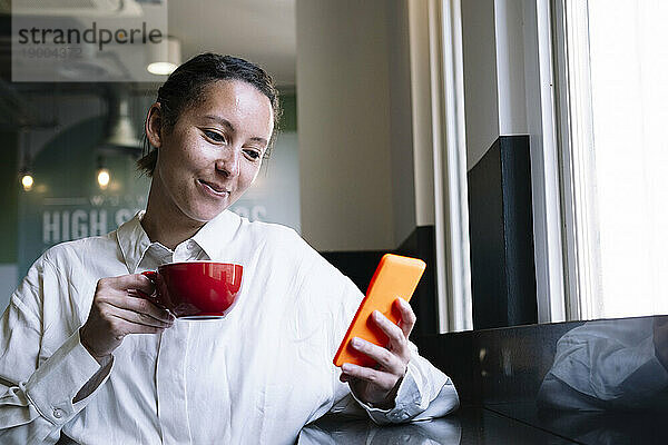 Lächelnde Geschäftsfrau hält Kaffee und Smartphone im Café