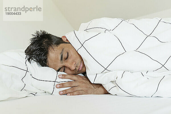 Young man wrapped in blanket sleeping at home