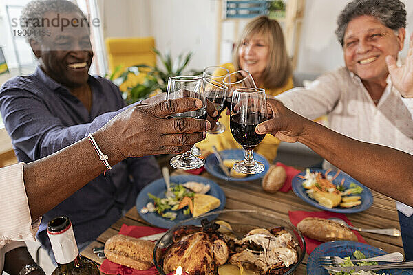 Fröhliche ältere Freunde stoßen bei einer Dinnerparty mit Weingläsern an