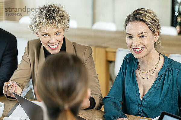 Glückliche Geschäftsfrau  die bei einem Treffen am Tisch mit Kollegen diskutiert