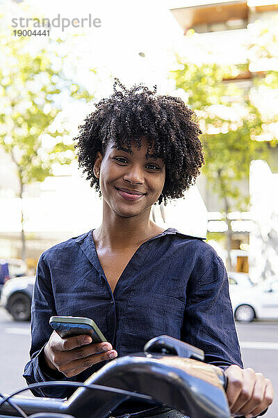 Lächelnde Frau mit Smartphone und Elektrofahrrad