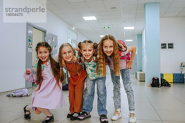 Fröhliche Schulmädchen stehen mit dem Arm um den Schulkorridor