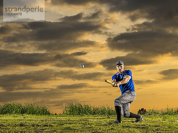 Mann in Sportkleidung schlägt in der Abenddämmerung mit Schläger auf Baseball ein