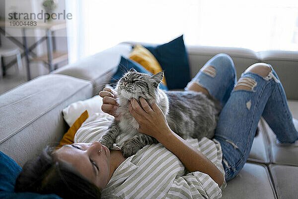 Frau liegt auf Sofa und streichelt Katze zu Hause