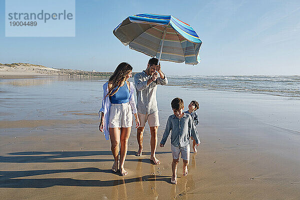 Father holding sunshade walking with family at beach