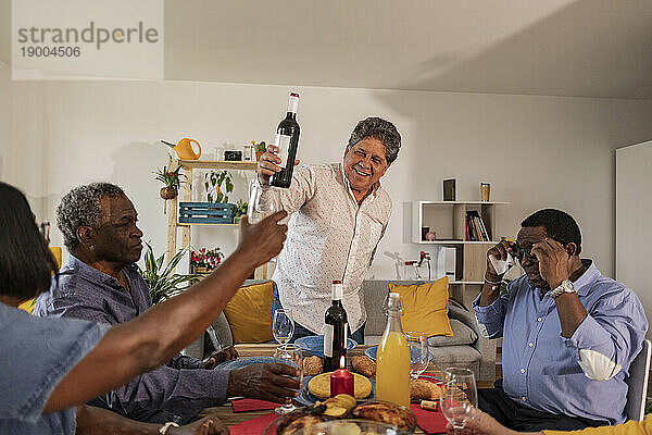 Älterer Mann serviert Wein an Freunde  die am Esstisch sitzen