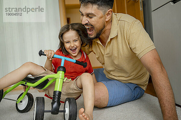 Glücklicher Vater spielt mit Sohn  der auf dem Fahrrad sitzt