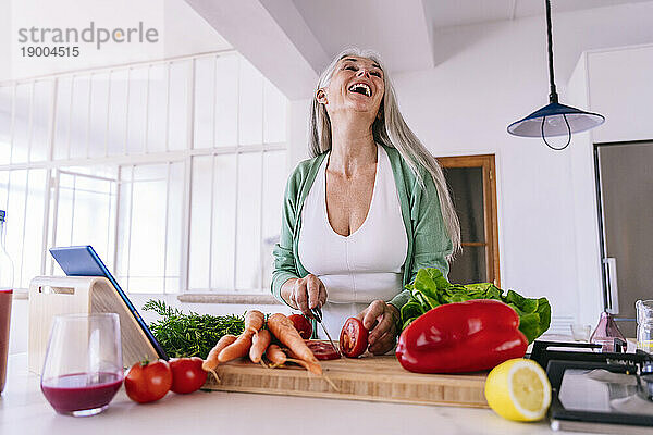 Fröhliche Frau schneidet zu Hause Tomaten mit Messer