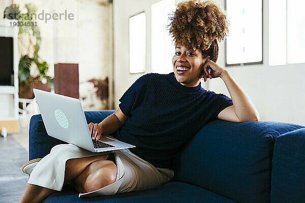Glückliche Geschäftsfrau sitzt mit Laptop auf dem Sofa im Büro