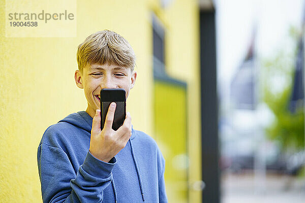 Fröhlicher blonder Junge spricht per Videoanruf vor gelber Wand