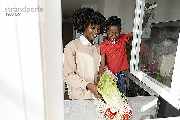 Glückliche Mutter und Sohn mit Lebensmitteln stehen zu Hause an der Küchentheke
