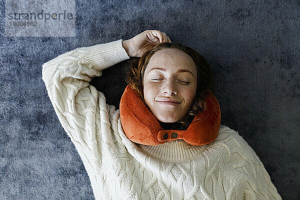 Smiling woman with neck pillow resting on carpet at home