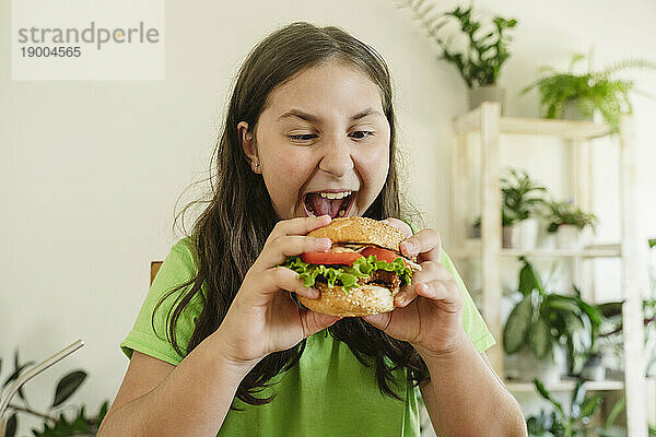 Mädchen hält Burger mit offenem Mund zu Hause