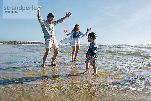 Eltern blicken mit ausgestreckten Armen auf ihren Sohn  der an einem sonnigen Tag am Strand genießt