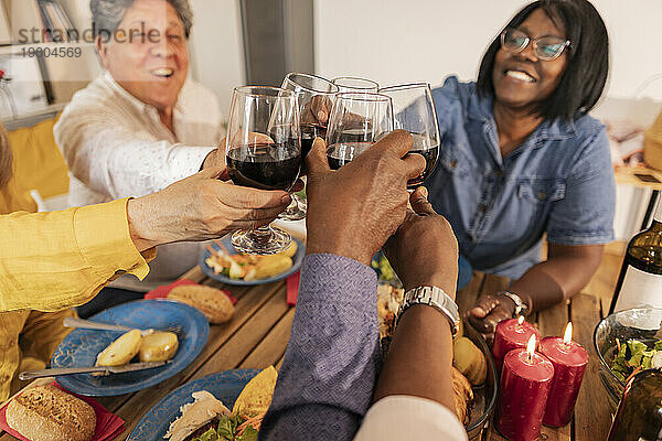 Fröhliche ältere Freunde stoßen bei einer Dinnerparty mit Weingläsern an