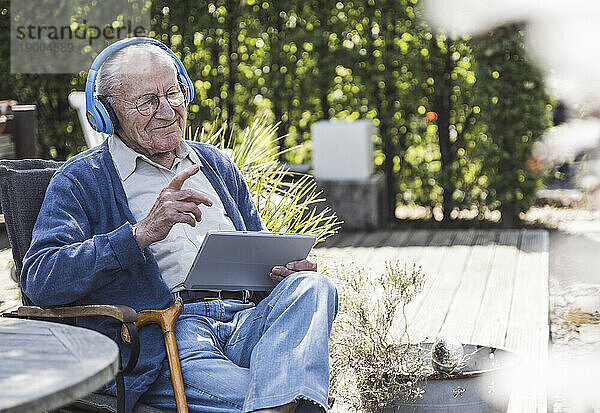 Nachdenklicher älterer Mann mit kabellosen Kopfhörern sitzt mit Tablet-PC