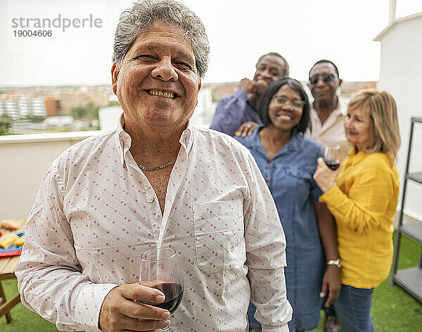 Glücklicher älterer Mann hält Weinglas mit Freunden im Hintergrund