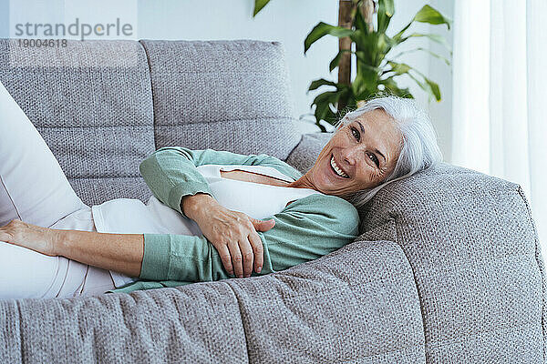 Glückliche Frau mit grauen Haaren entspannt sich zu Hause auf dem Sofa