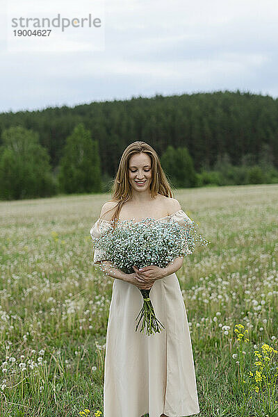 Lächelnde junge Frau hält Blumenstrauß auf dem Feld