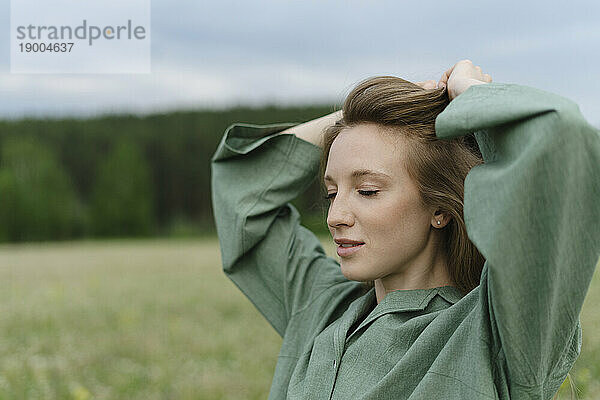 Beautiful young woman tying hair on field