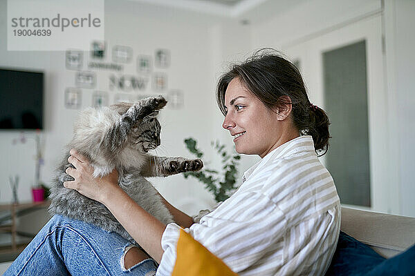 Glückliche Frau streichelt Katze auf Sofa zu Hause