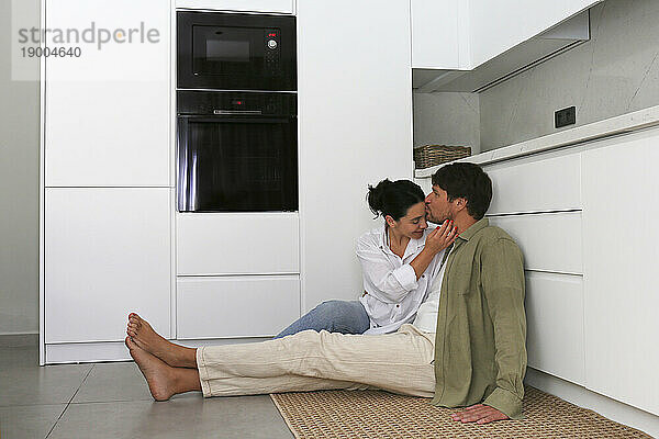 Man kissing woman sitting in kitchen at home