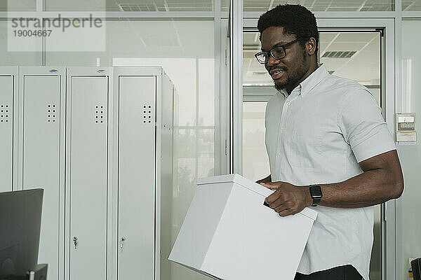 Young businessman carrying box at office