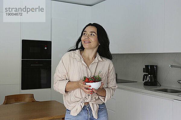 Nachdenkliche Frau hält eine Schüssel Erdbeeren in der heimischen Küche