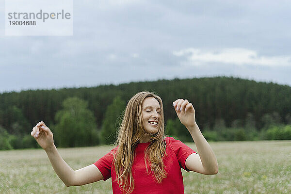 Lächelnde junge Frau im roten T-Shirt  die auf dem Feld tanzt