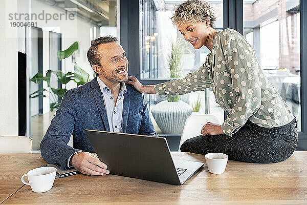 Fröhliche Geschäftskollegen diskutieren am Laptop in der Bürokantine