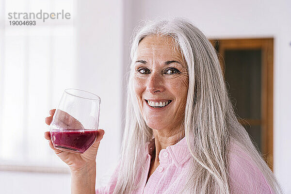 Glückliche Frau hält zu Hause ein Glas mit gesundem Saft