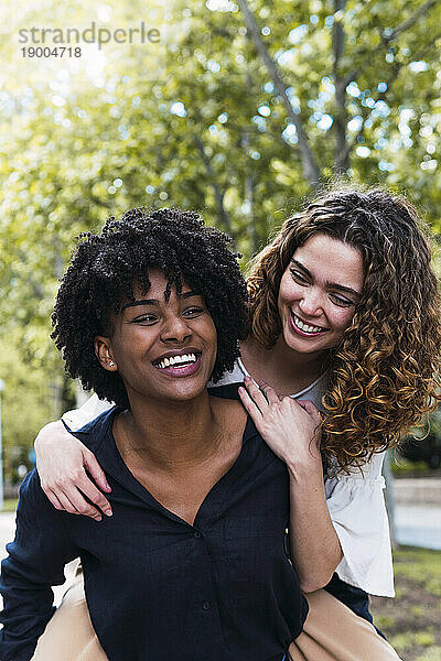 Happy young woman giving piggyback ride to friend in park