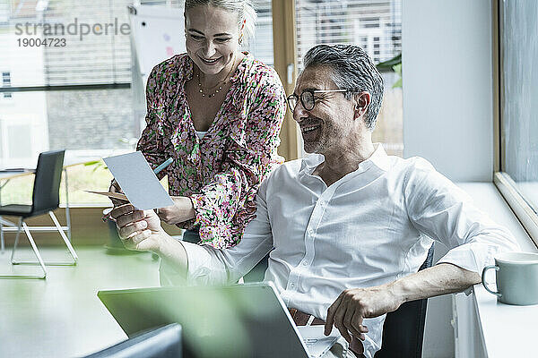 Lächelnde Geschäftsfrau und Geschäftsmann betrachten Foto im Büro