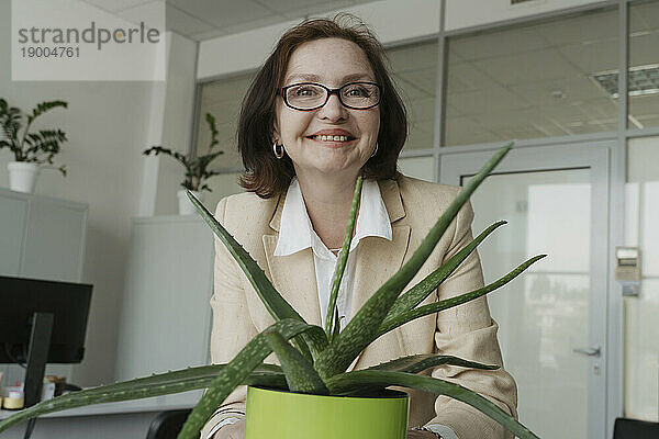 Lächelnde ältere Geschäftsfrau hält Aloe-Vera-Pflanze im Büro