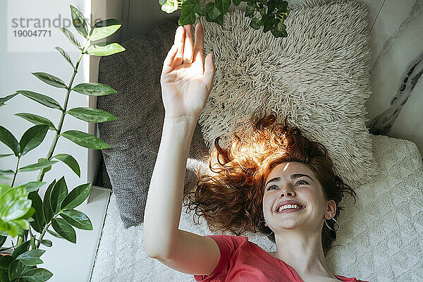 Happy young woman touching plant at home