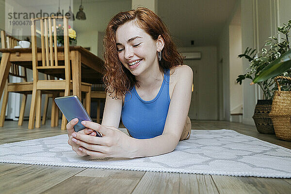 Glückliche junge Frau  die zu Hause ihr Smartphone auf dem Teppich benutzt