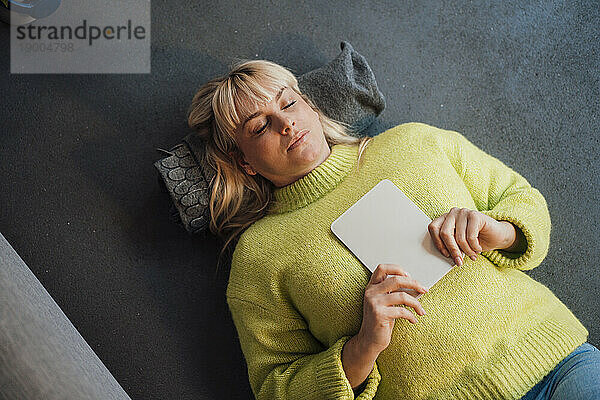 Woman with eyes closed lying on floor with tablet PC