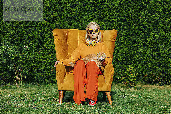 Blonde Frau mit Sonnenbrille sitzt mit Katze auf einem Stuhl