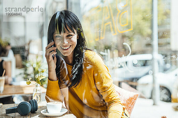 Glückliche reife Frau  die im Café mit dem Smartphone spricht