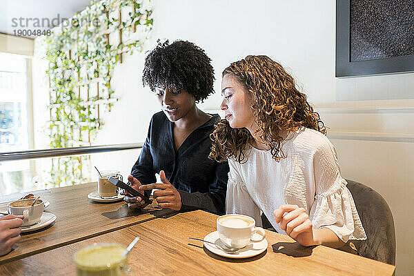Frau mit Freundin benutzt Smartphone im Café