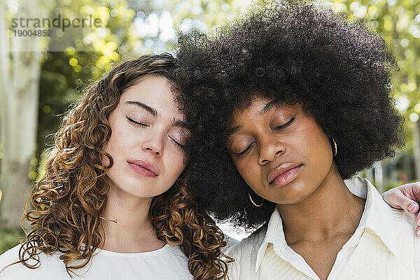 Multiracial friends with eyes closed in park