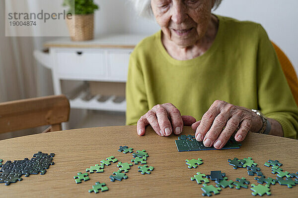 Ältere Frau löst zu Hause Puzzle auf dem Tisch