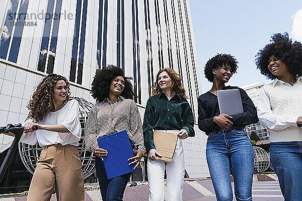 Glückliche Geschäftsfrauen  die gemeinsam im Büropark spazieren gehen