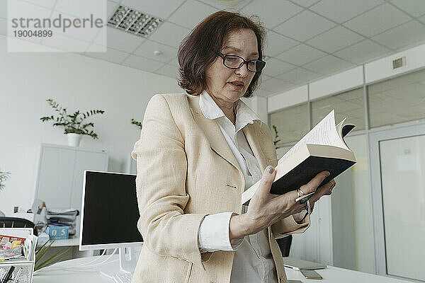 Ältere Geschäftsfrau liest Buch im Büro