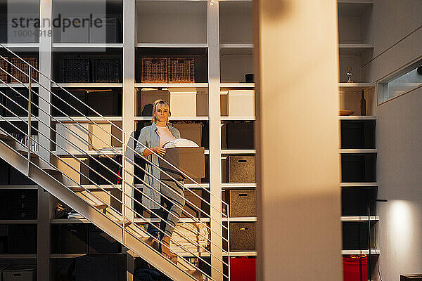 Frau steht mit Kiste vor Regal im Treppenhaus