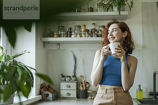 Smiling young woman standing with coffee cup at home