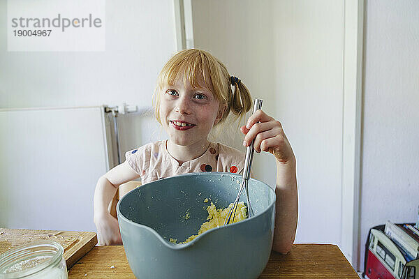 Smiling girl making cake batter using wire whisk at home
