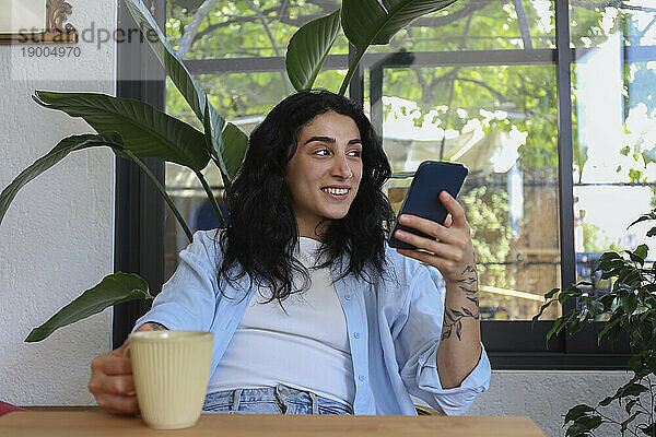 Glückliche Frau hält Mobiltelefon im Café