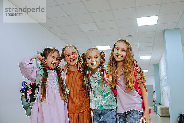 Glückliche Schulmädchen stehen mit dem Arm um den Schulkorridor