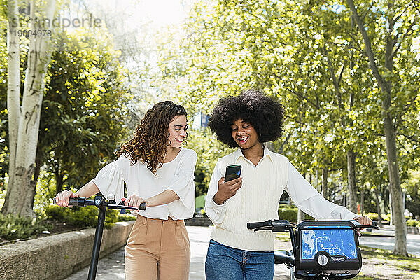 Glückliche Frau mit Freundin  die Smartphone im Park benutzt